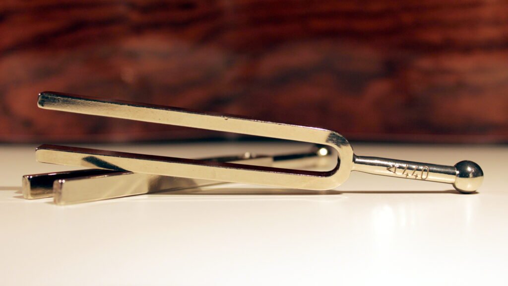 two steel tuning forks on a white desk with the side of a classical guitar as a background, the tuning forks let the tone a be heard